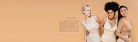 Téléchargez les photos : Happy african american model in underwear embracing pretty interracial women isolated on beige, banner - en image libre de droit
