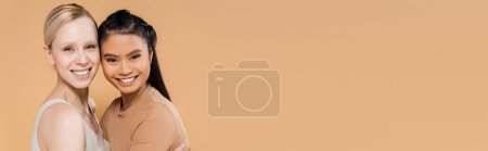 Téléchargez les photos : Jeunes et heureux modèles interracial en sous-vêtements souriant à la caméra isolé sur beige, bannière - en image libre de droit