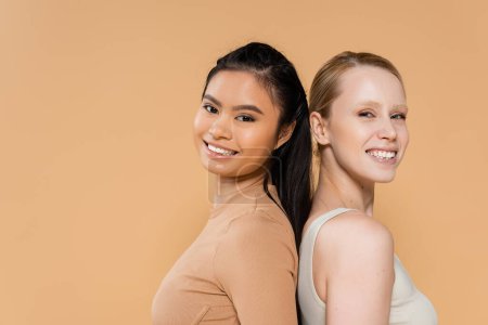 Téléchargez les photos : Pretty multiethnic women in underwear posing back to back and smiling at camera isolated on beige - en image libre de droit