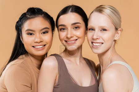 mujeres bastante multiétnicas en lencería sonriendo a la cámara aislada en beige