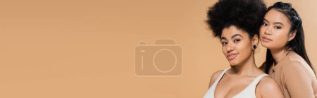 Téléchargez les photos : Heureuses femmes multiethniques en lingerie souriant à la caméra isolée sur beige, bannière - en image libre de droit