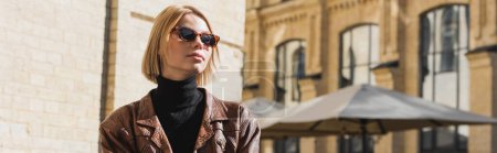 blonde woman in sunglasses and stylish leather jacket sitting in outdoor cafe, banner