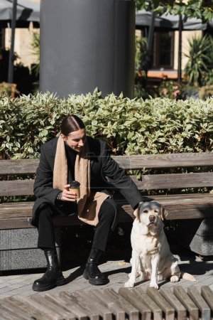 full length of happy tattooed man in coat holding takeaway drink and cuddling labrador  puzzle 642379386