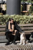 full length of happy tattooed man in coat holding takeaway drink and cuddling labrador  Poster #642379386