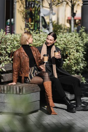 volle Länge des glücklichen Paares hält Pappbecher mit Kaffee to go, während es auf der Bank sitzt 