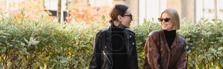 happy and stylish couple in sunglasses and leather jackets looking at each other outdoors during date, banner