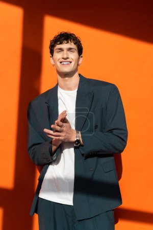 Lächelnder Mann in stylischem Outfit blickt in die Kamera auf orangefarbenem Hintergrund mit Sonnenlicht 