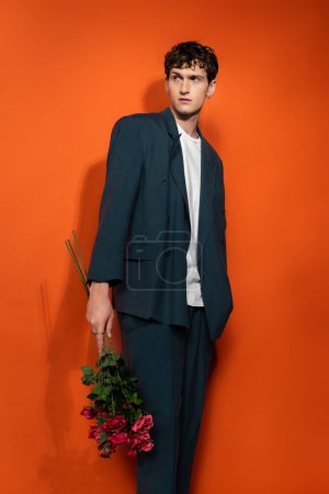 Stylish model in blue suit holding roses on orange background 