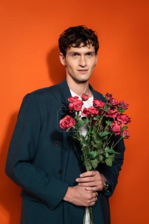 Portrait of smiling man in blue jacket holding roses on red background 