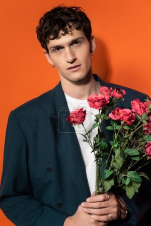 Photo for Portrait of man in jacket and t-shirt holding roses on orange background - Royalty Free Image