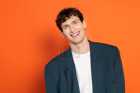 Foto de Hombre positivo en chaqueta azul y camiseta mirando a la cámara sobre fondo naranja - Imagen libre de derechos