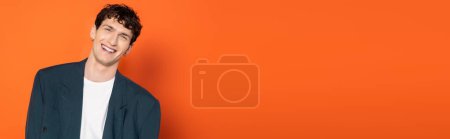 Téléchargez les photos : Smiling man in blue jacket and t-shirt looking at camera on orange background, banner - en image libre de droit