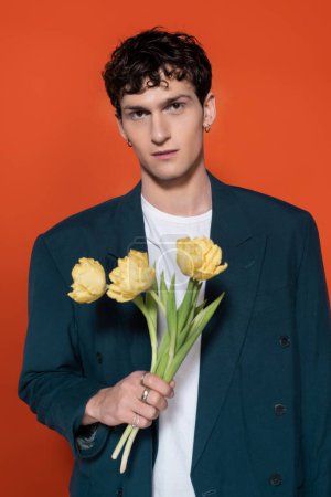 Photo for Portrait of stylish brunette man holding yellow tulips isolated on red - Royalty Free Image