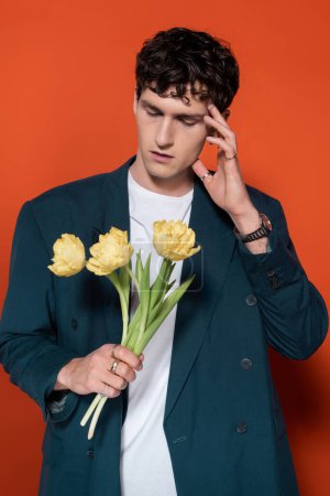 Trendy model in jacket holding tulips on red background 