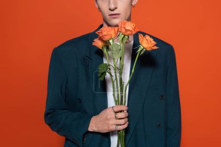 Cropped view of trendy model holding orange roses for 8 march isolated on red 