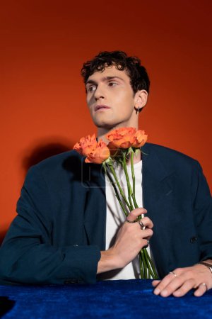 Photo for Curly man in blazer and t-shirt holding orange flowers on red background - Royalty Free Image