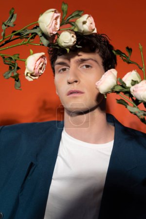 Téléchargez les photos : Portrait of stylish man looking at camera near roses on red background - en image libre de droit