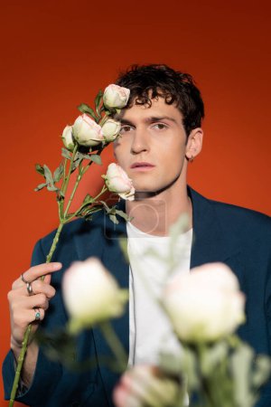 Trendige lockige Mann mit weißen Rosen auf rotem Hintergrund