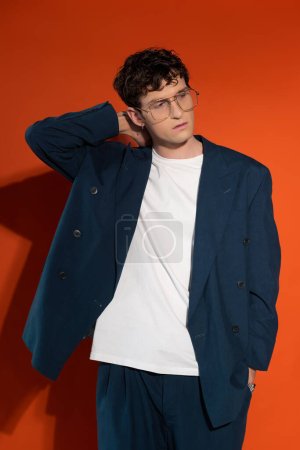 Stylish model in eyeglasses and blue suit posing on red background