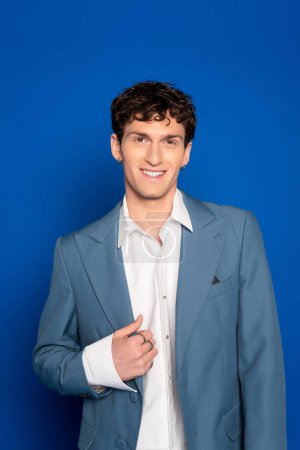 Porträt eines lockigen Mannes in Jacke und Hemd, der in die Kamera auf blauem Hintergrund blickt 