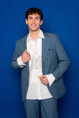 Lockiger Mann im schicken Anzug lächelt in die Kamera auf blauem Hintergrund 