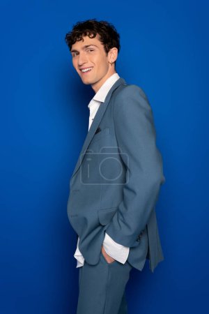 Positive model in suit and shite shirt looking at camera on blue background 