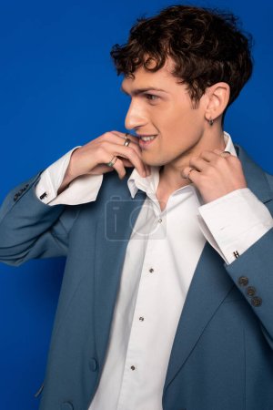 Portrait of smiling man adjusting collar of shirt on blue background 