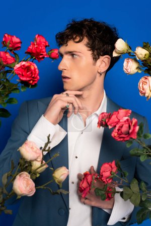 Trendy curly model posing near white and red roses on blue background 