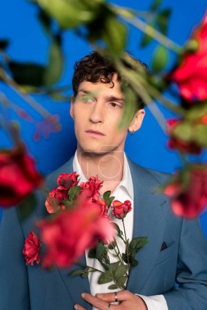 Young model in jacket and shirt holding rose flowers on blue background 