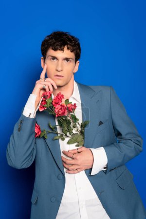 Modelo elegante en camisa y chaqueta con flores y posando sobre fondo azul 