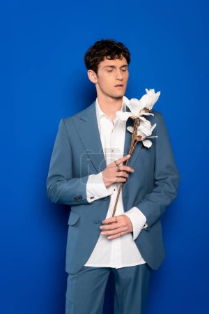 Trendiger junger Mann mit Magnolienblüten auf blauem Hintergrund 