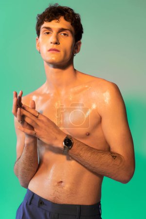 Stylish man with oil on body looking at camera on green background 
