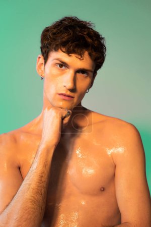 Young man with oil on skin looking at camera on green background 