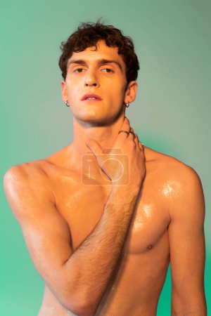 Portrait of stylish brunette man with oil on skin touching neck on green background