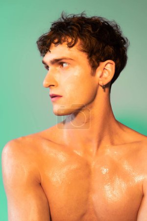 Portrait of shirtless brunette model with oil on skin looking away on green background