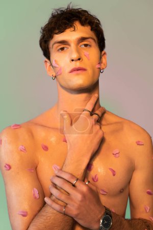 Shirtless man with petals on body touching neck on colorful background 