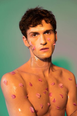 Portrait of young man with petals on body looking at camera on colorful background 