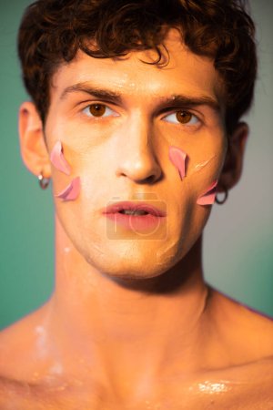Portrait of man with petals on face looking at camera on colorful background 