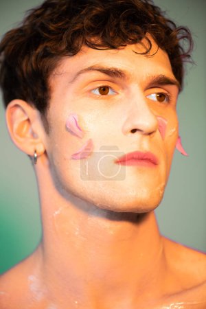 Portrait of young man with petals on face looking away on colorful background 