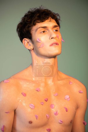 Shirtless man with petals on body standing on colorful background 