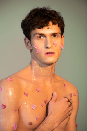 Téléchargez les photos : Portrait d'homme torse nu avec des pétales sur le corps et le visage sur fond coloré - en image libre de droit