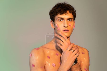 Young man with petals on body touching face on colorful background 
