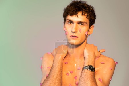 Brunette man with petals on body looking at camera on colorful background 