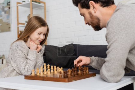 bearded man moving chess figure while playing with smiling daughter at home