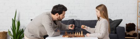 Téléchargez les photos : Side view of father and daughter holding figures while playing chess in living room, banner - en image libre de droit