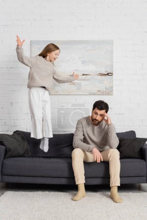 cheerful girl showing wow gesture and jumping on couch near tired dad