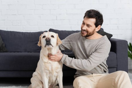 Téléchargez les photos : Heureux homme barbu embrassant chien labrador à la maison - en image libre de droit