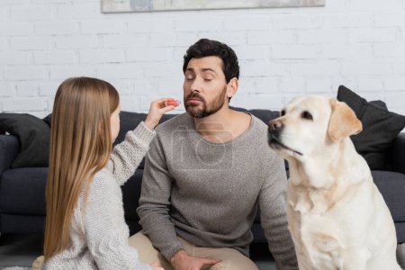 preteen girl holding lip gloss while playing with bearded father near labrador dog