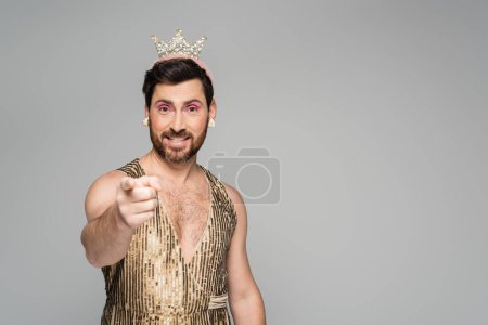 fröhlicher Mann mit Spielzeugkrone auf dem Kopf und Prinzessinnen-Kostüm, das mit dem Finger auf Grau zeigt 