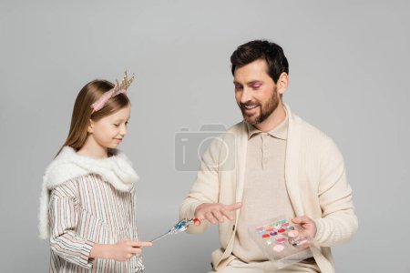 cheerful kid in crown holding toy wand near ring of father while playing game isolated on grey 